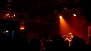 Saxofonist cântând pe o scenă iluminată în club de jazz.