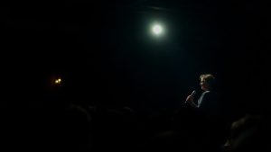 Poet pe scena iluminata, citind cu pasiune.